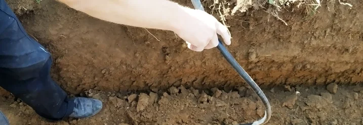 Person verlegt schwarzes Kabel in einem Graben.